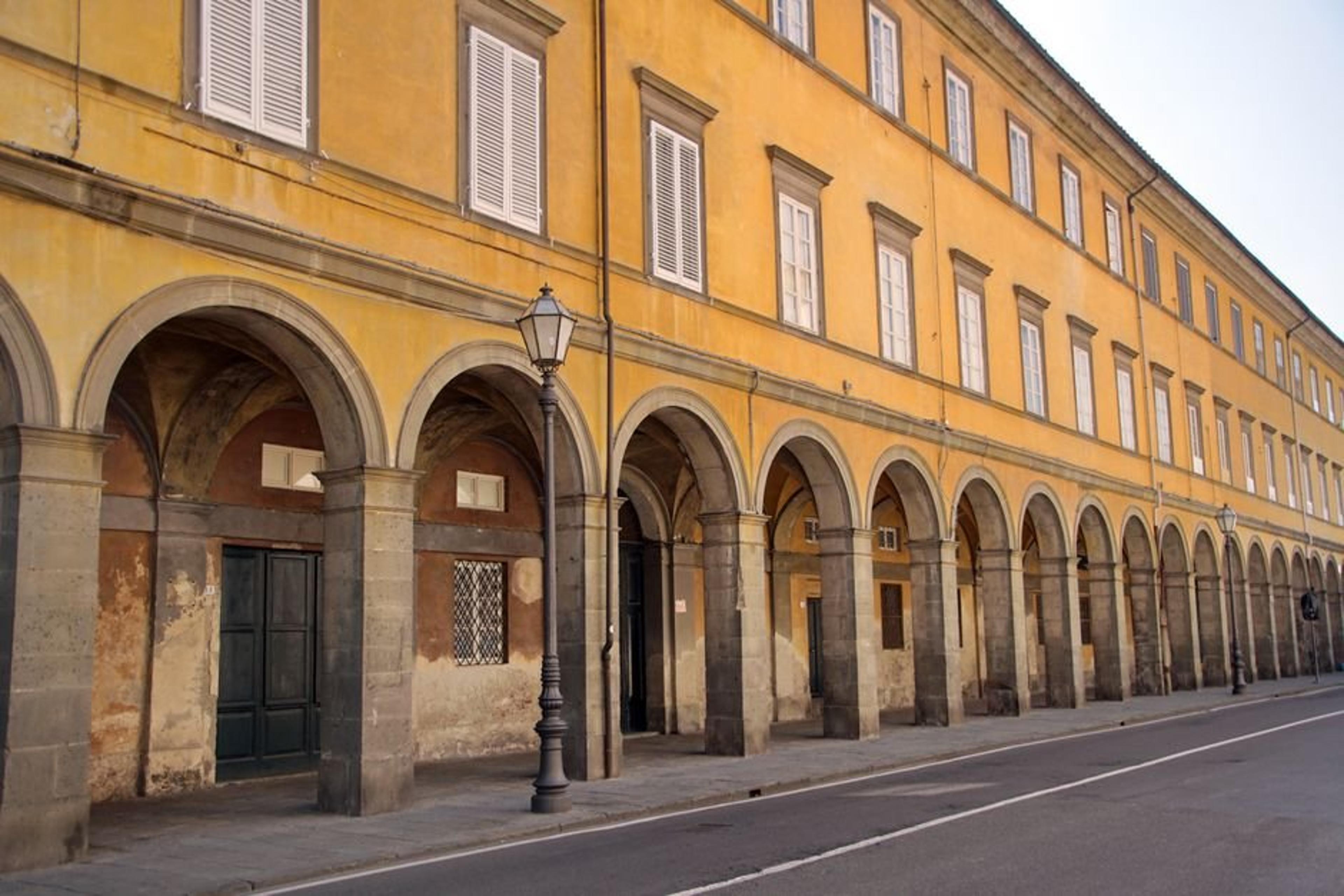 Yellow building with colonnades and street lamps in urban area, reflecting classical architecture.